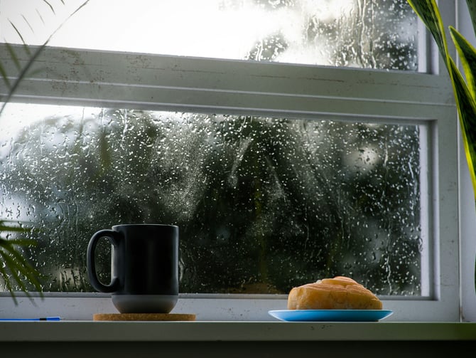 Coffee mug and pastry on a rainy windowsill